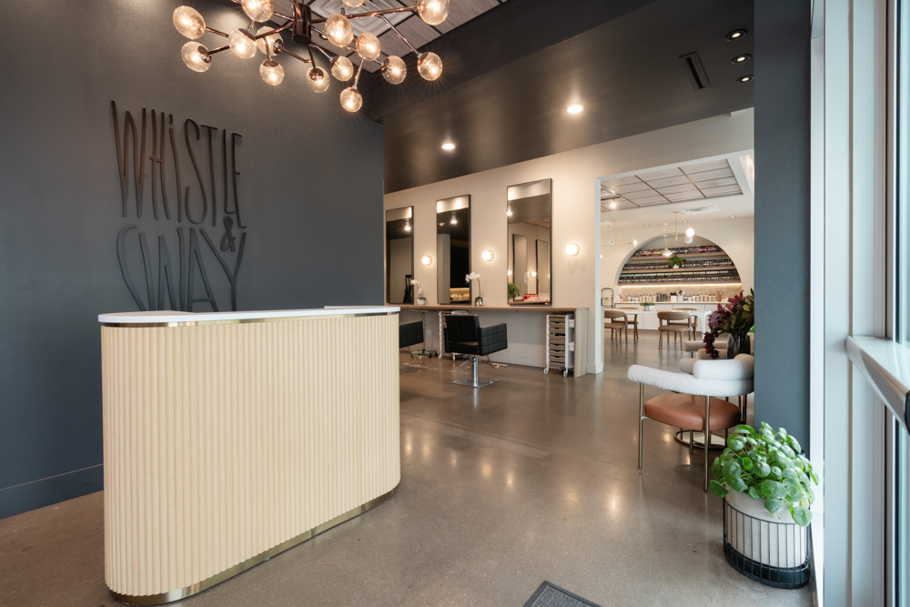 The entry seen whole — logo wall, fluted desk and the styling floor beyond