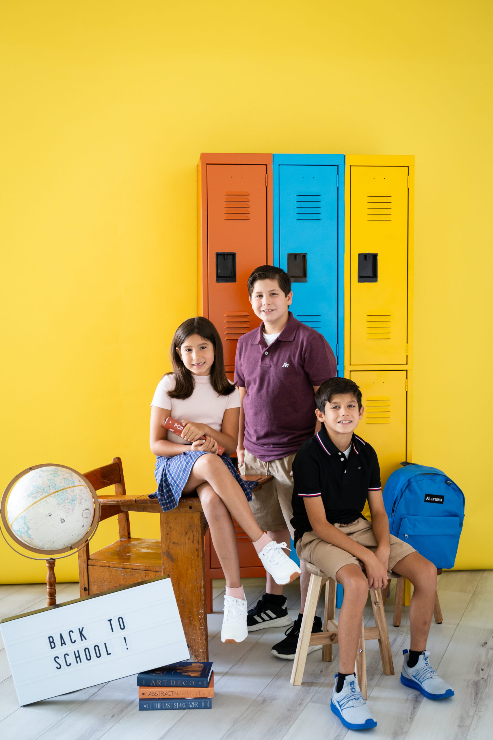 Three stylish siblings pose during a back to school mini session at Lightly Photography's Fort Worth studio, each showing off their unique personality in front of a colorful school-themed set.